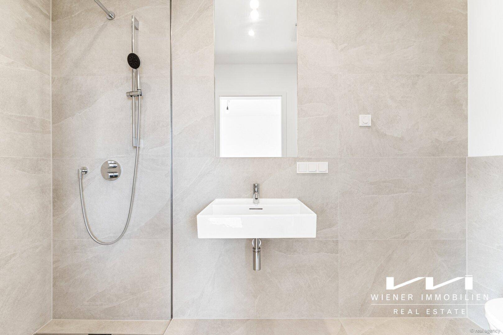 Modernes Badezimmer mit ebenerdiger Dusche und Einzelwaschbecken, gefliest in hellen Grautönen.