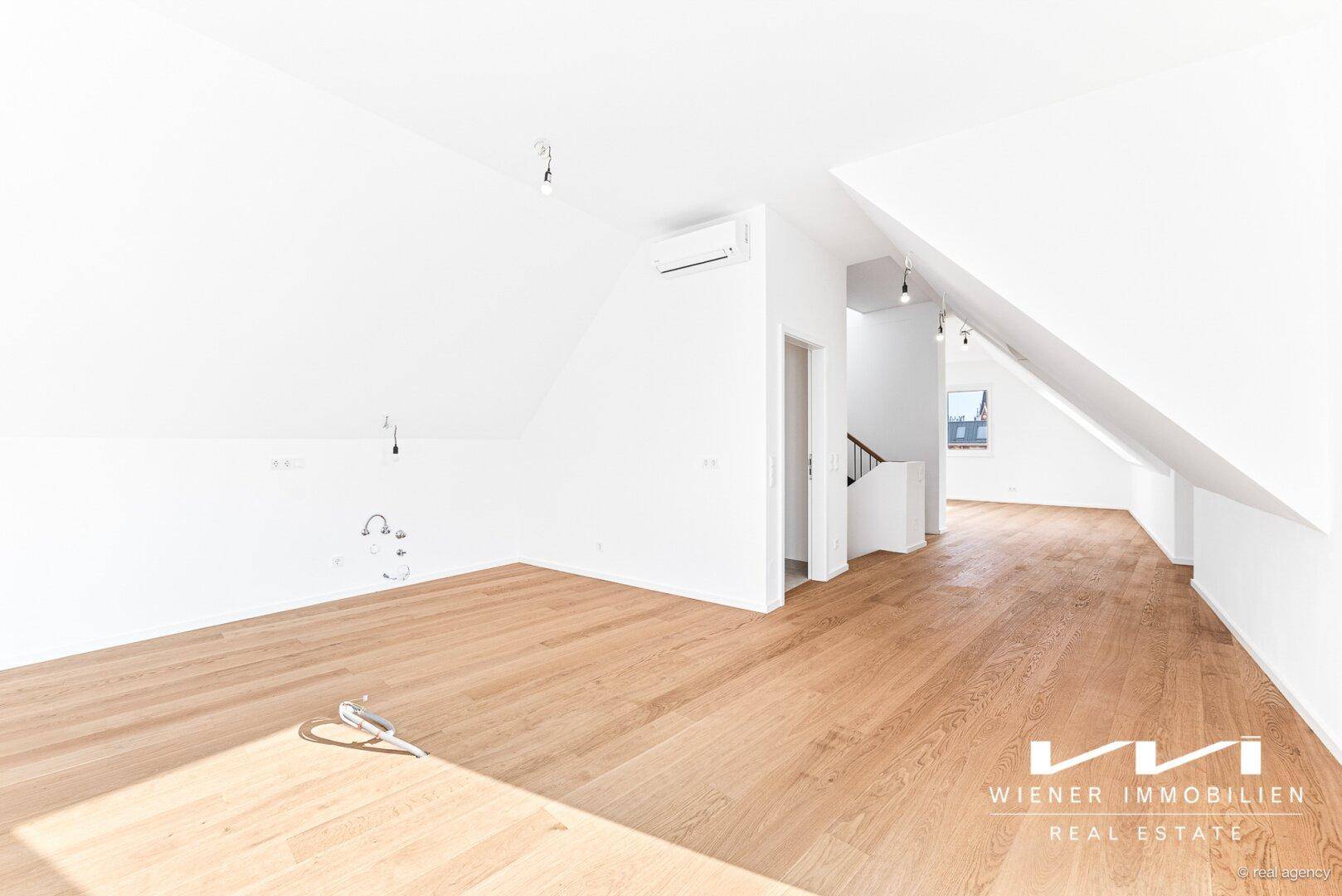 Geräumiger Wohnbereich im Dachgeschoss mit Holzparkettboden, Dachschrägen und Klimaanlage.