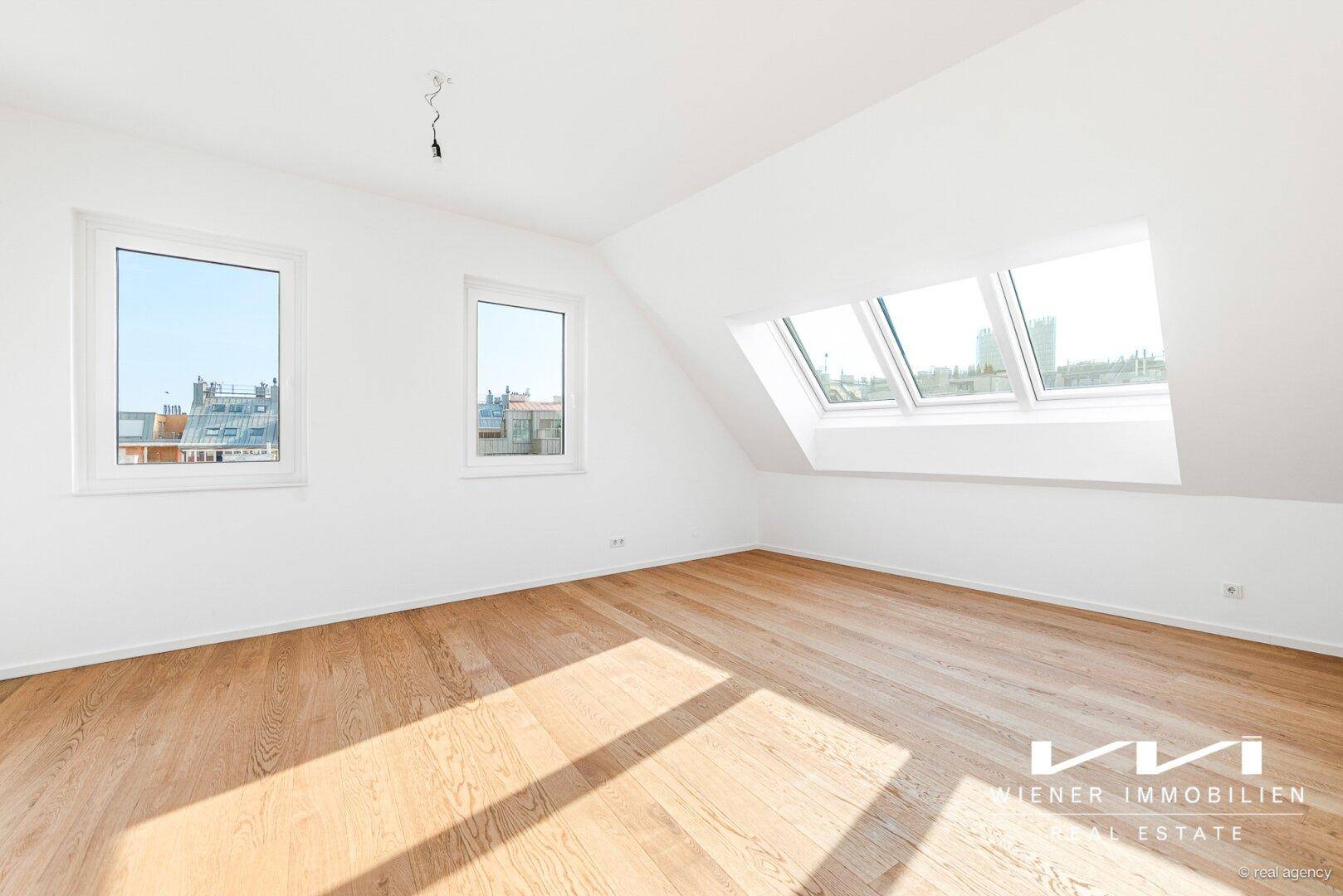 Helles Schlafzimmer im Dachgeschoss mit Parkettboden, Dachfenstern und Blick auf die Stadt.
