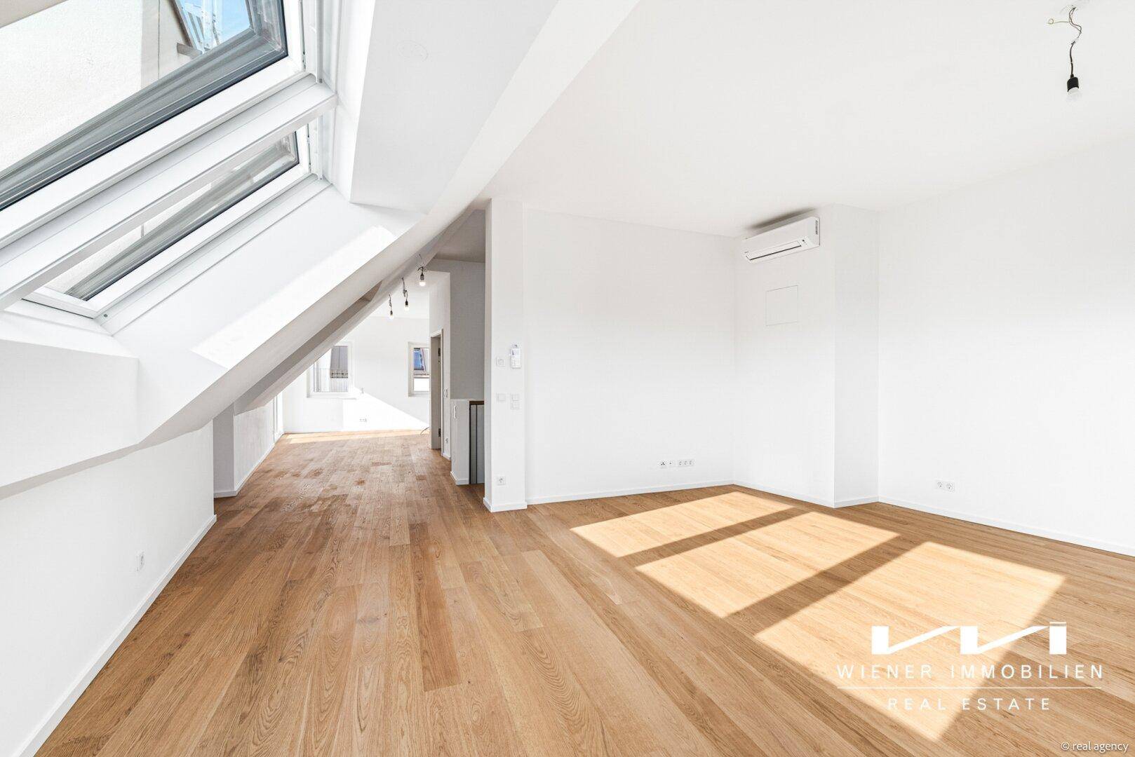 Geräumiger Wohnbereich im Dachgeschoss mit Holzparkettboden, großen Dachfenstern und Klimaanlage.