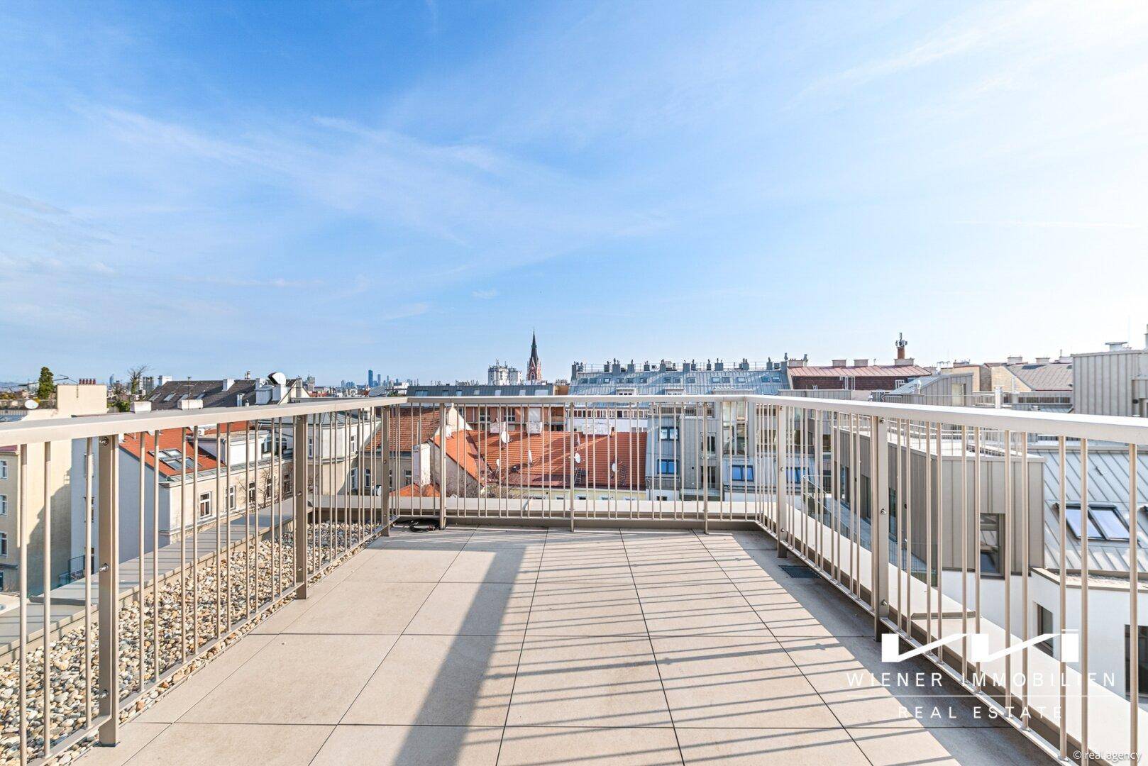 Weitläufige Dachterrasse mit Fliesenboden und Panoramablick über die Dächer der Stadt.