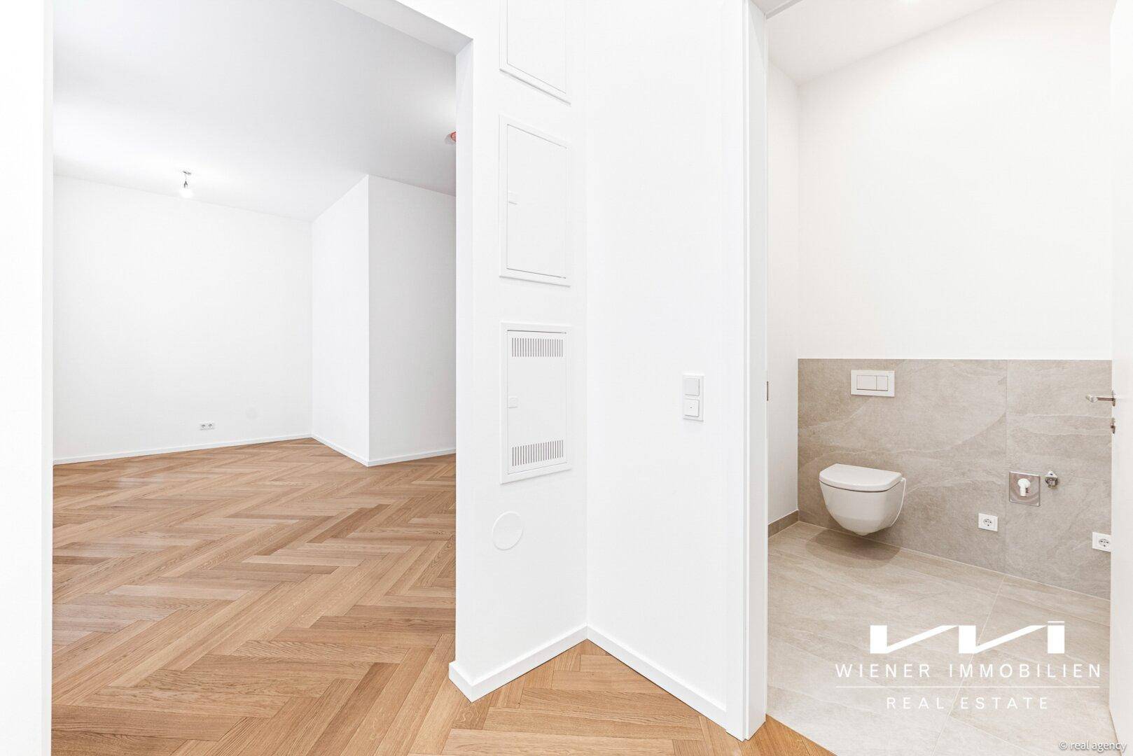 Separates WC mit wandhängender Toilette und modernen beigefarbenen Fliesen, sauber und funktional gestaltet.