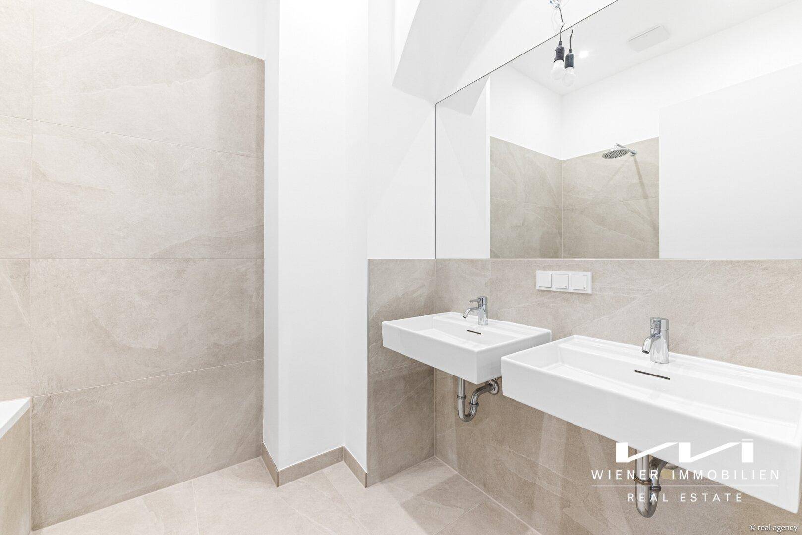 Modernes Badezimmer mit Doppelwaschbecken, großem Spiegel und beigefarbenen Fliesen an Wänden und Boden.
