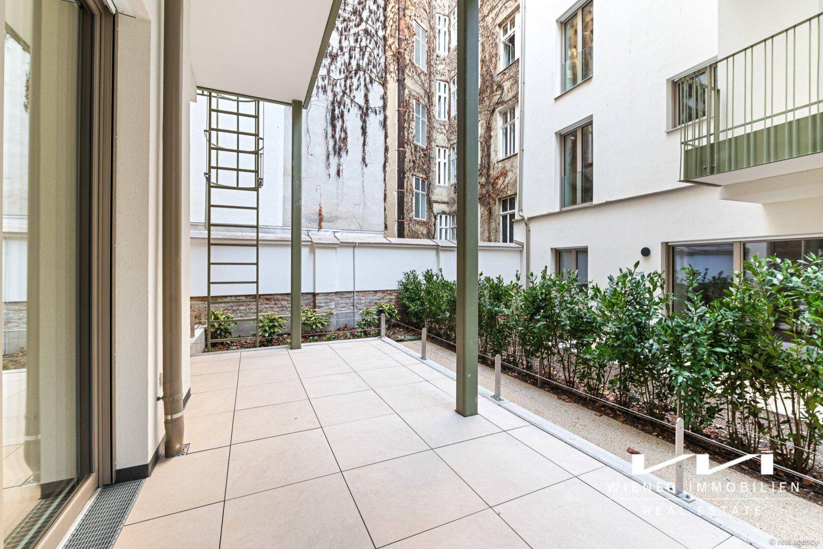 Geräumige Terrasse mit Fliesenboden und Blick auf den begrünten Innenhof, ideal für Entspannung.