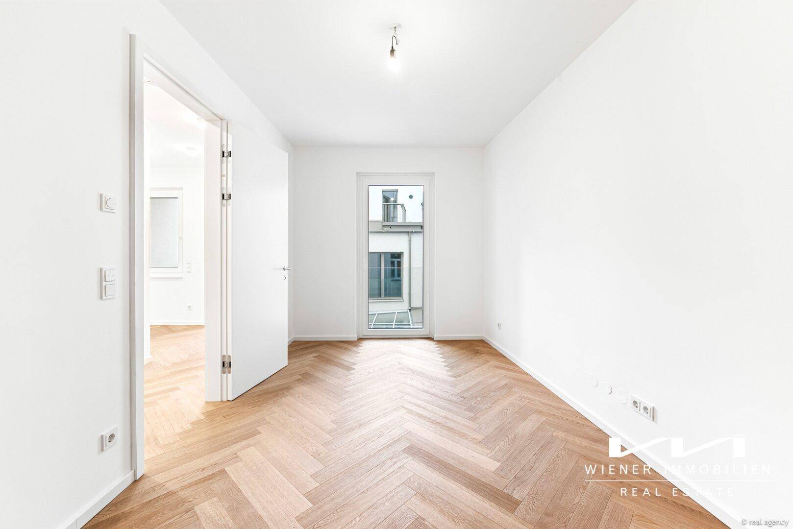 Helles Schlafzimmer mit Fischgrätparkett und Zugang zu einem französischen Balkon.