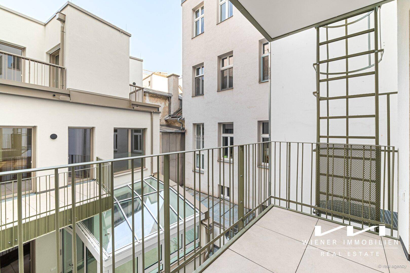 Balkon mit Metallgeländer und Blick auf den ruhigen Innenhof der Wohnanlage.
