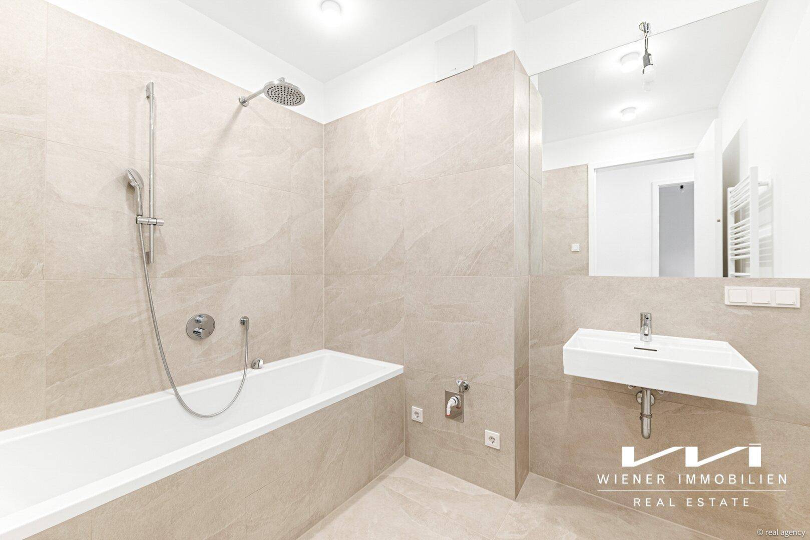 Modernes Badezimmer mit Badewanne, Regendusche, Einzelwaschbecken und beigefarbenen Fliesen.
