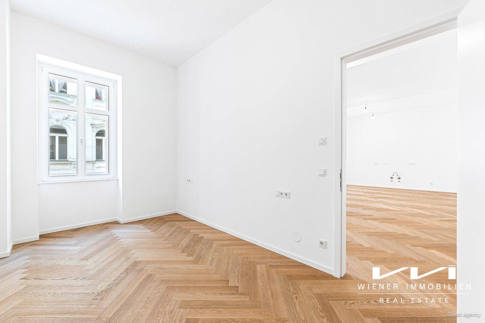 Ruhiges Zimmer mit Fischgrätparkett und Fenster, das einen Blick auf die umliegenden Gebäude bietet.