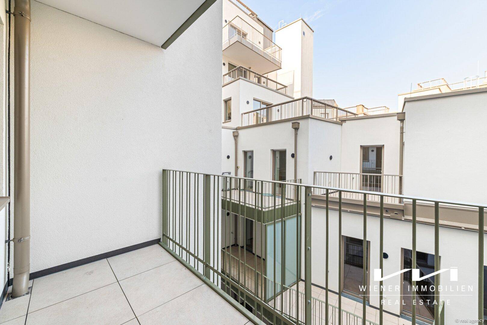 Moderner Balkon mit Fliesenboden und Blick auf den Innenhof des Gebäudes.