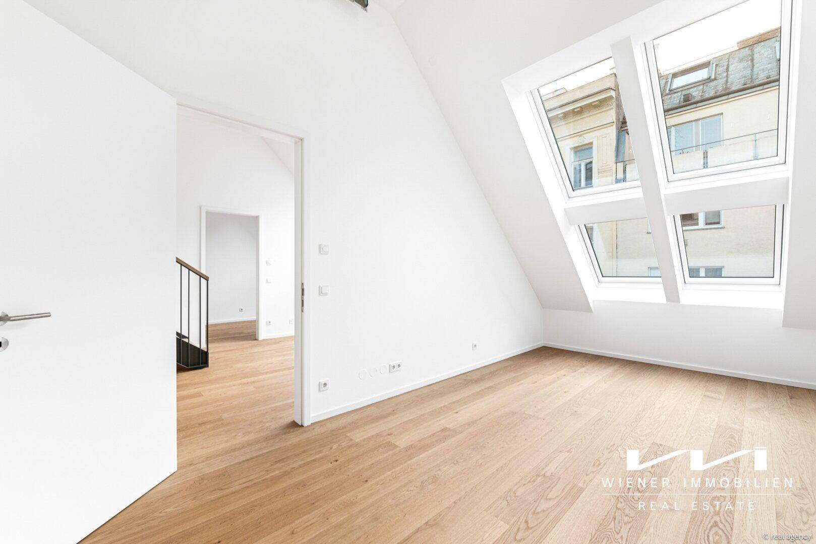 Helles Dachgeschosszimmer mit Holzfußboden, großen Dachfenstern und Blick auf die Umgebung.