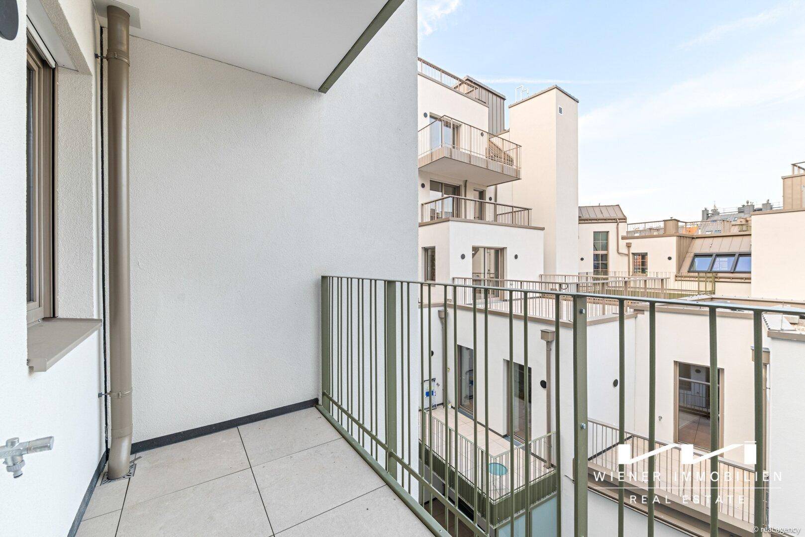 Heller Balkon mit Metallgeländer und Blick auf den Innenhof der Wohnanlage.