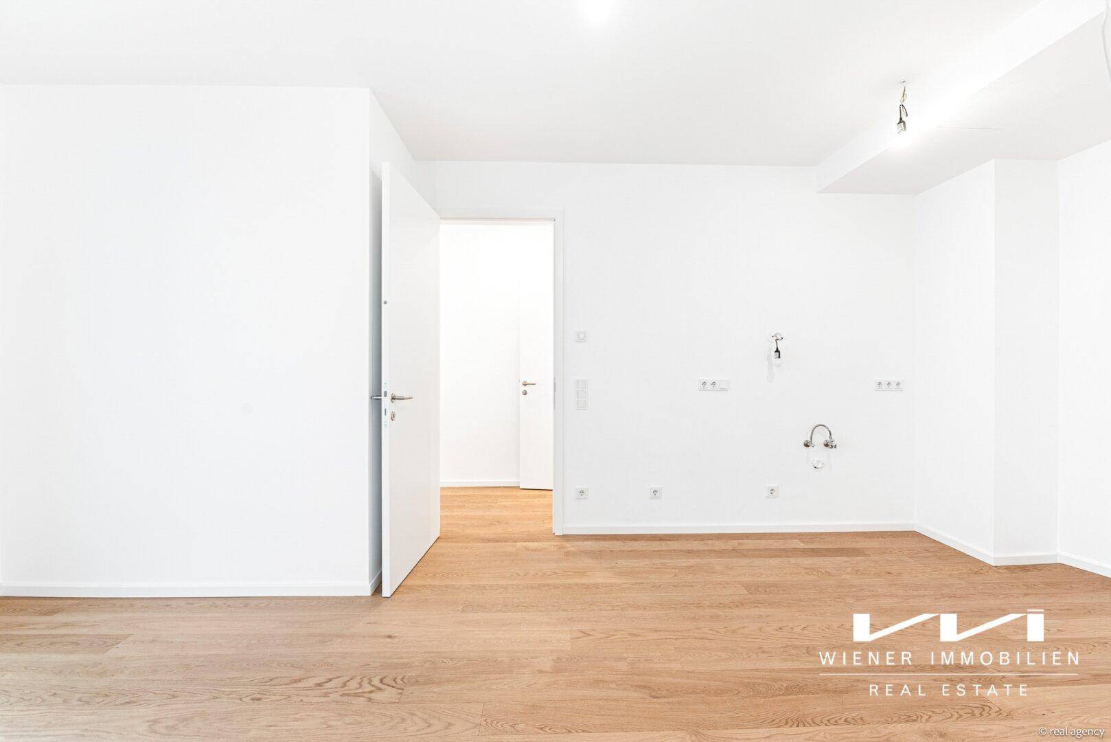 Leerer Raum mit Holzfußboden und vorbereiteten Anschlüssen für eine Küche.