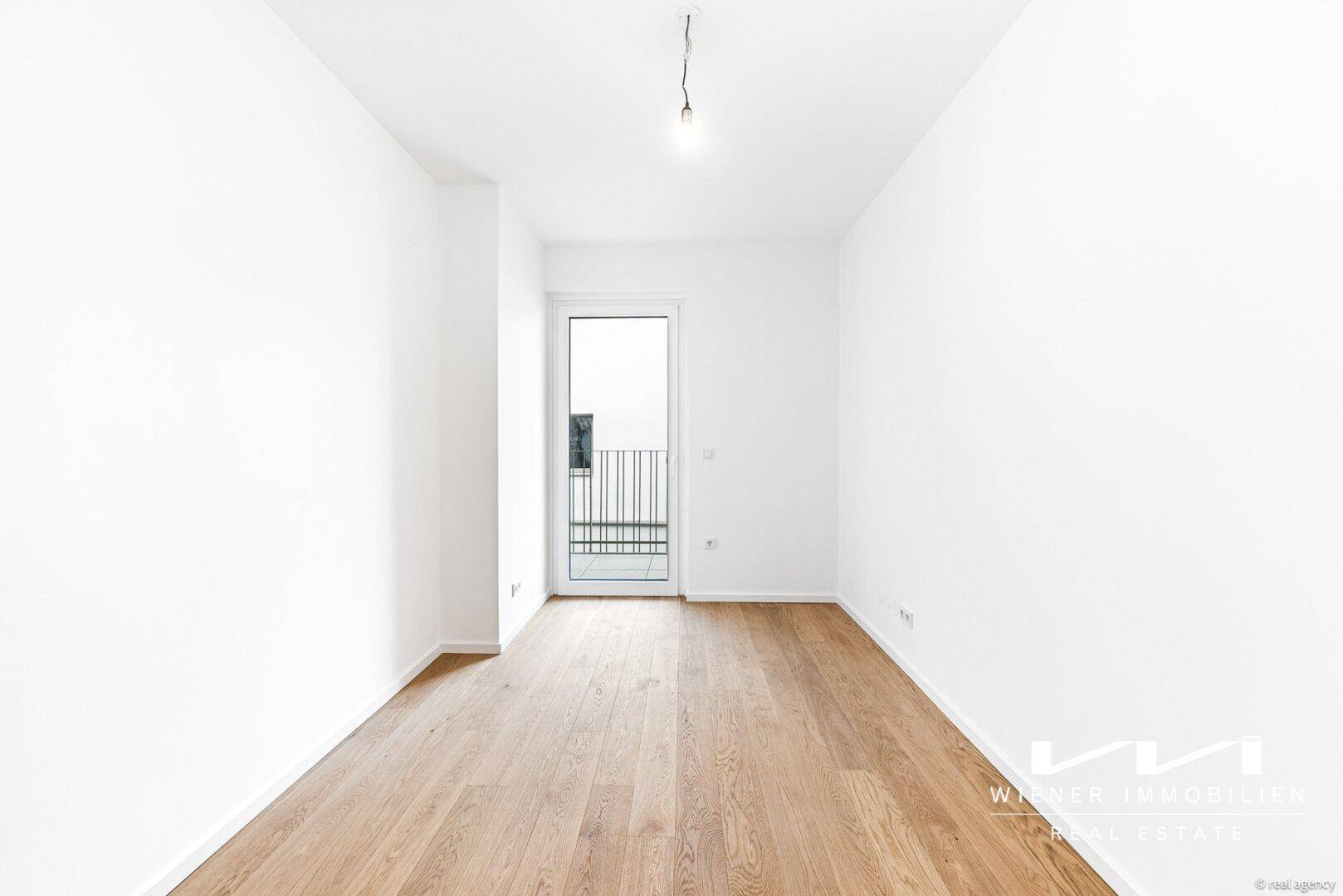 Heller Raum mit Parkettboden und Zugang zu einem kleinen Balkon.