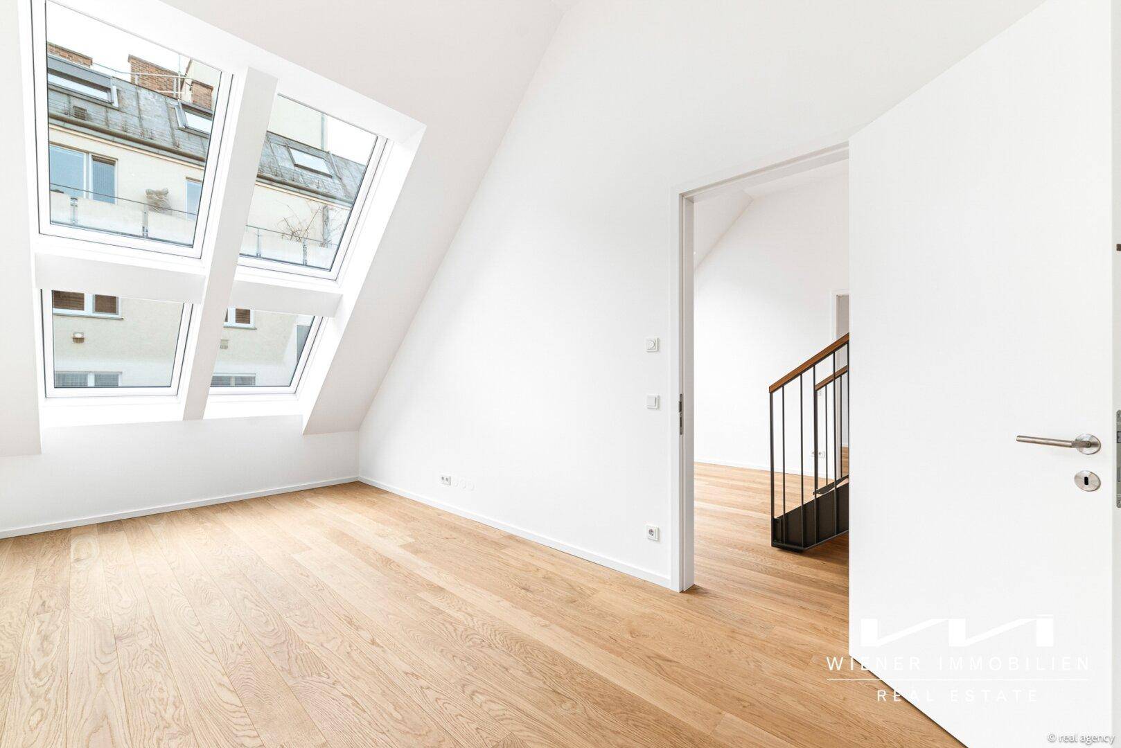 Lichtdurchfluteter Dachraum mit Holzfußboden, schrägen Wänden und Blick auf die Treppe.