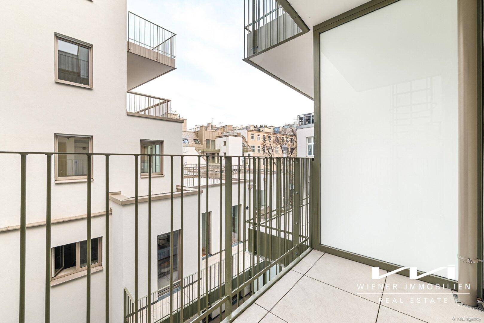 Balkon mit Fliesenboden und Metallgeländer, umgeben von städtischer Architektur.