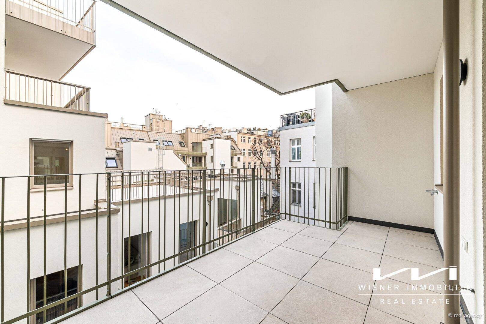 Geräumiger Balkon mit Fliesenboden und Blick auf die umliegenden Gebäude.