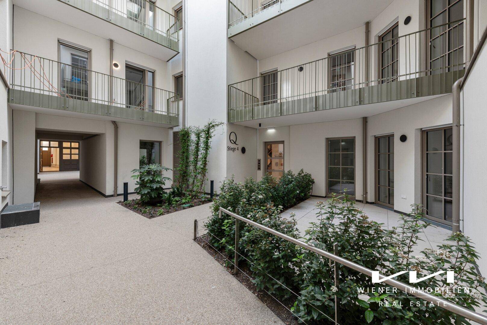 Heller Innenhof eines modernen Wohngebäudes mit Zugang zu den Wohnungen und kleinen Grünflächen.