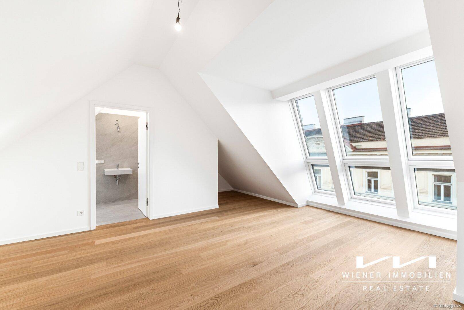 Helles Schlafzimmer im Dachgeschoss mit Parkettboden, schrägen Wänden und großen Dachfenstern.