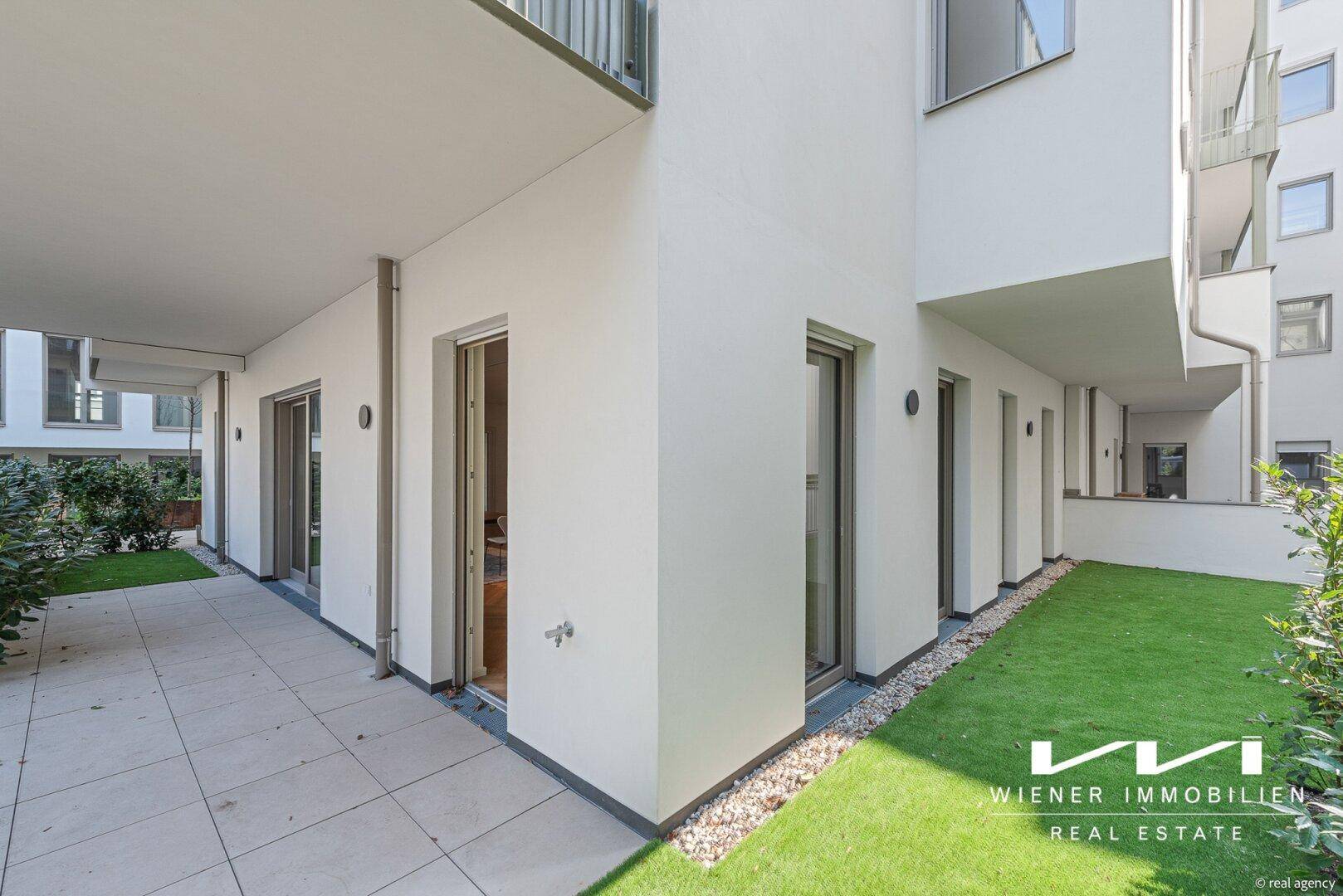Moderne Terrasse im Erdgeschoss mit angrenzender Rasenfläche und Zugang zu den Wohnräumen.