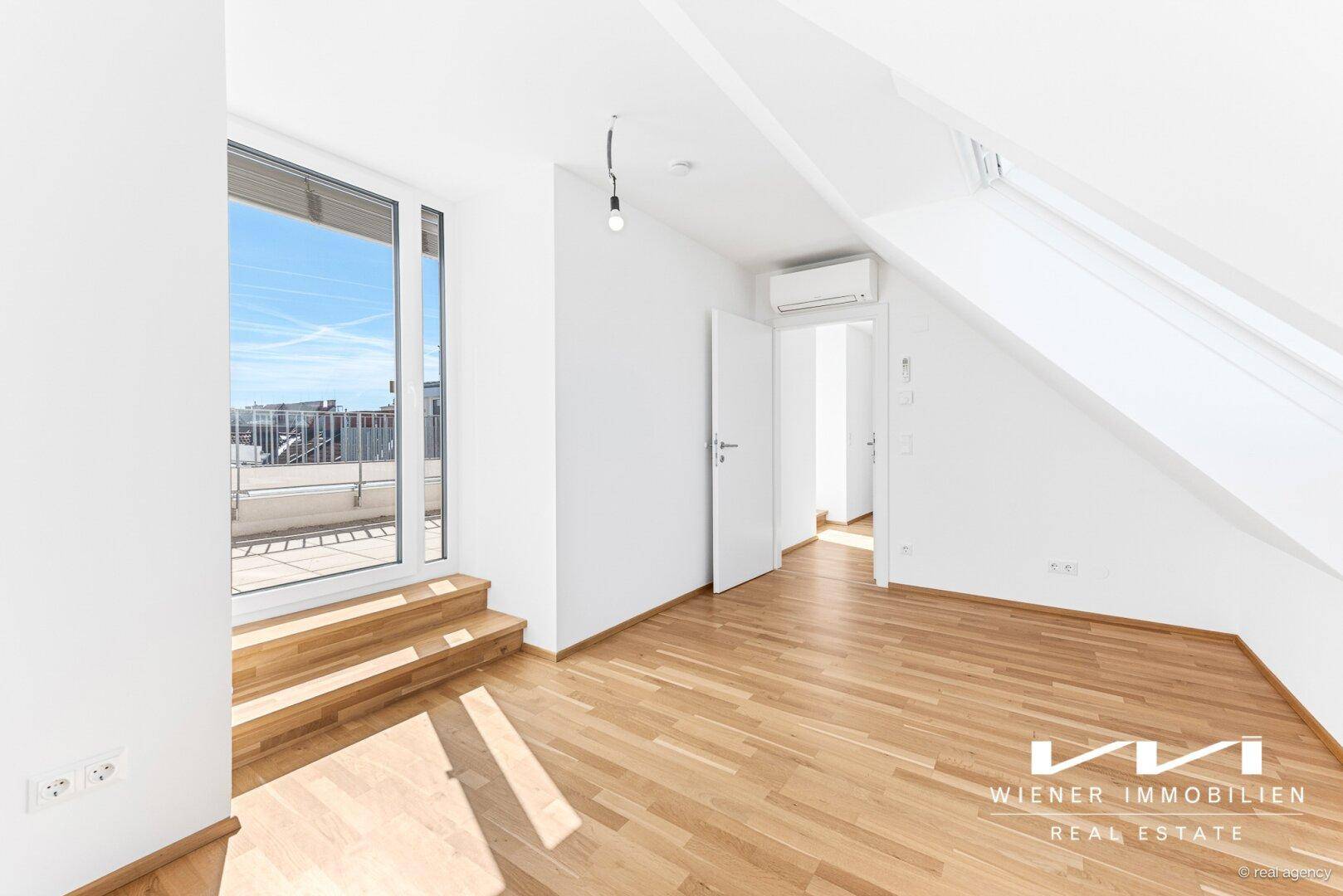 Heller Raum mit Holzboden, Dachschrägen und großem Terrassenzugang, der viel Licht bietet.
