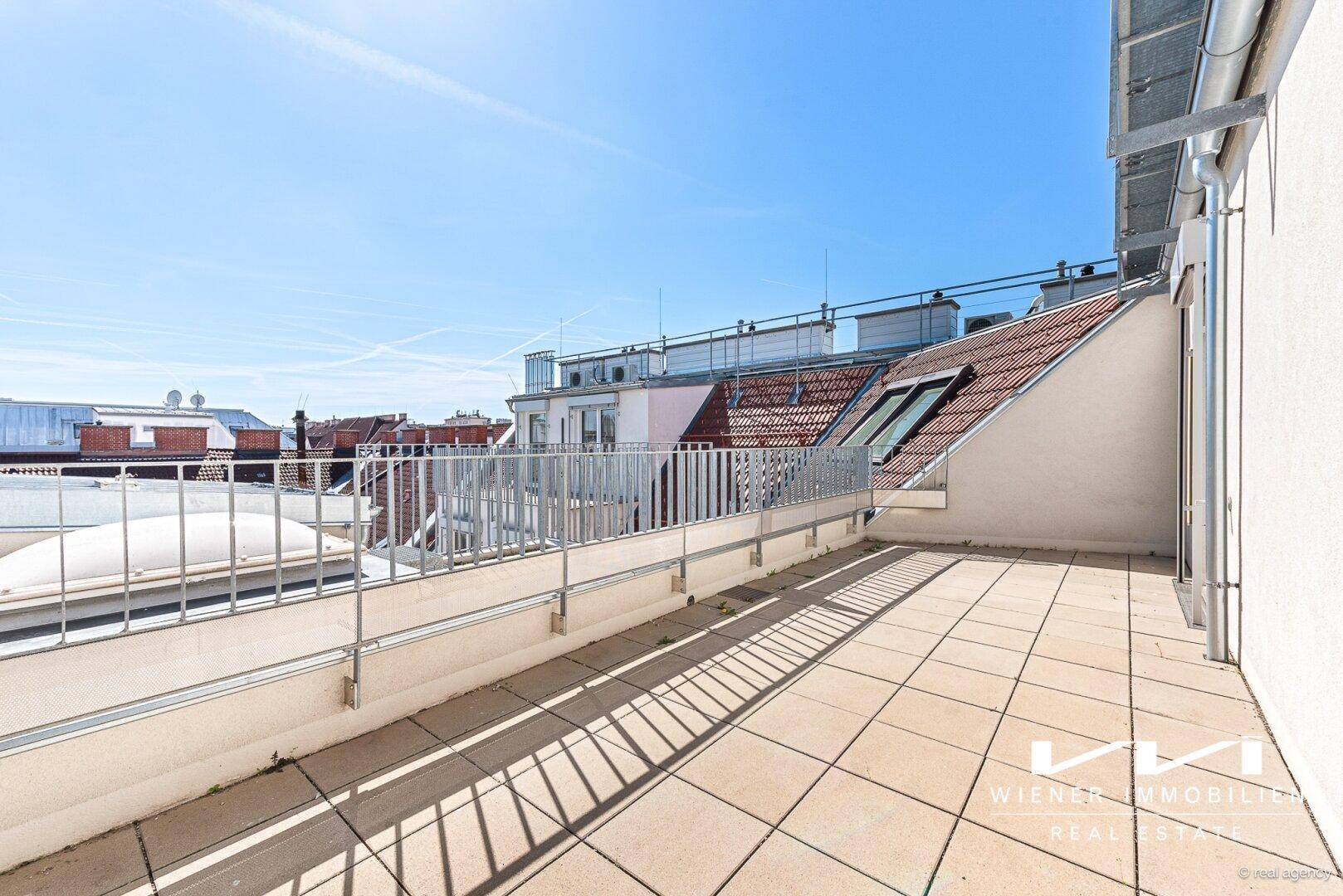 Weitläufige Dachterrasse mit Fliesenboden und Metallgeländer, bietet einen weiten Blick über die Dächer.