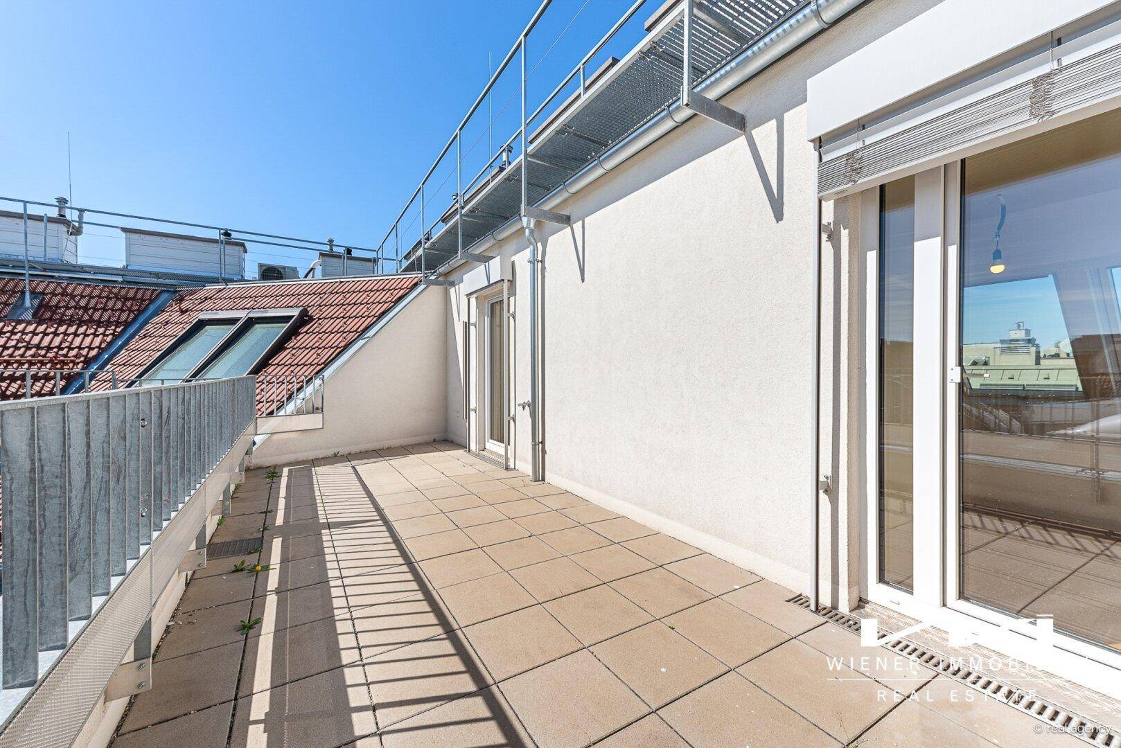 Sonnige Dachterrasse mit Fliesenboden und Zugang zu den Innenräumen, ideal zum Entspannen im Freien.