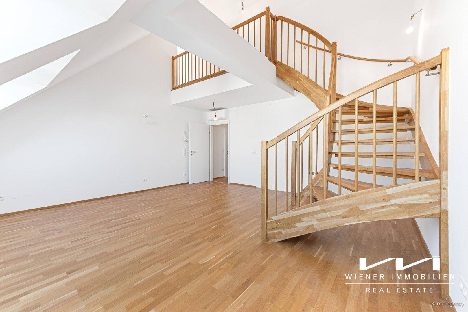 Heller Wohnraum mit eleganter Holzwendeltreppe und Dachschrägen, die zu einem weiteren Stockwerk führt.