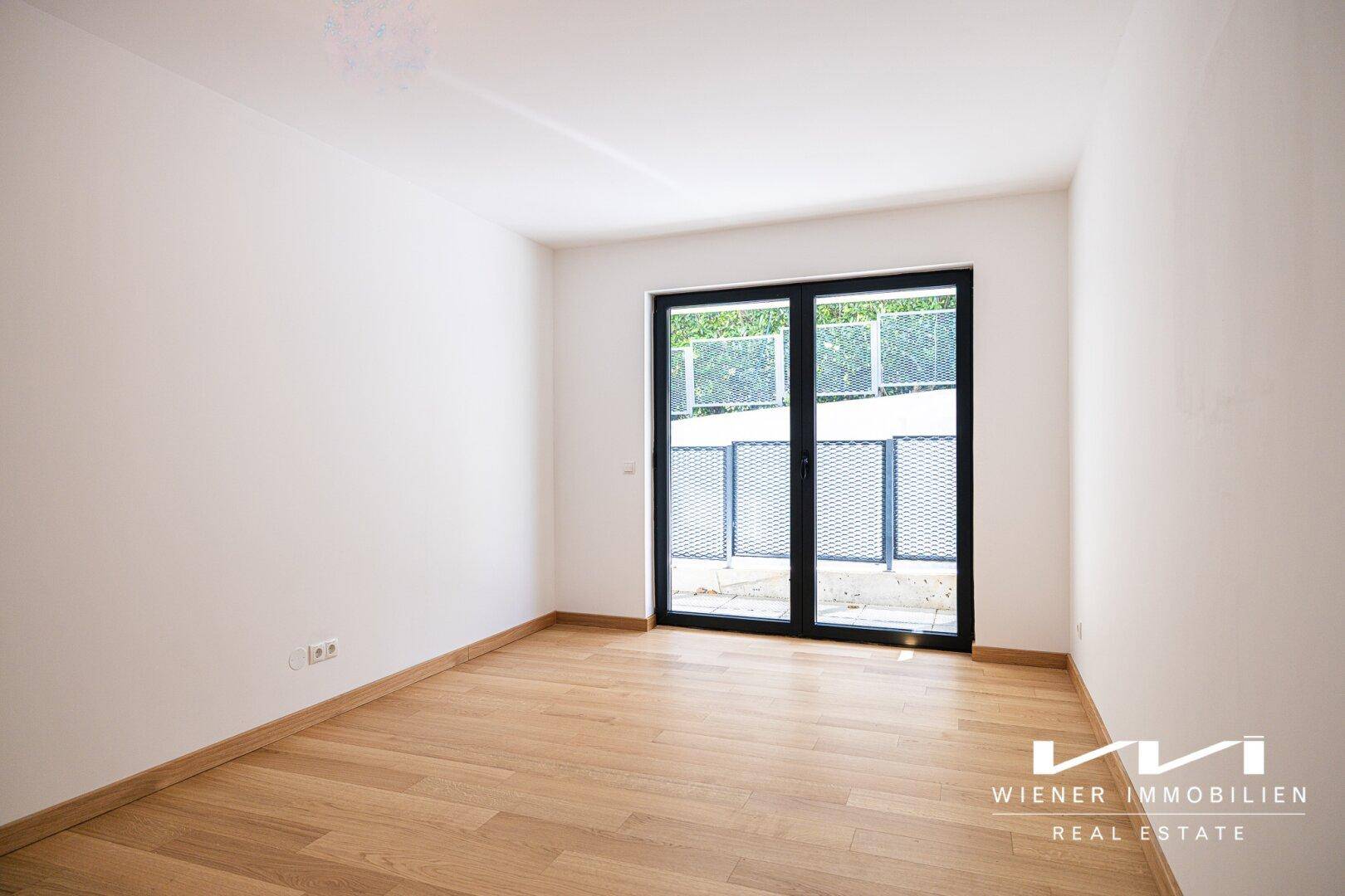 Helles Zimmer mit Parkettboden und Zugang zu einem kleinen Außenbereich.