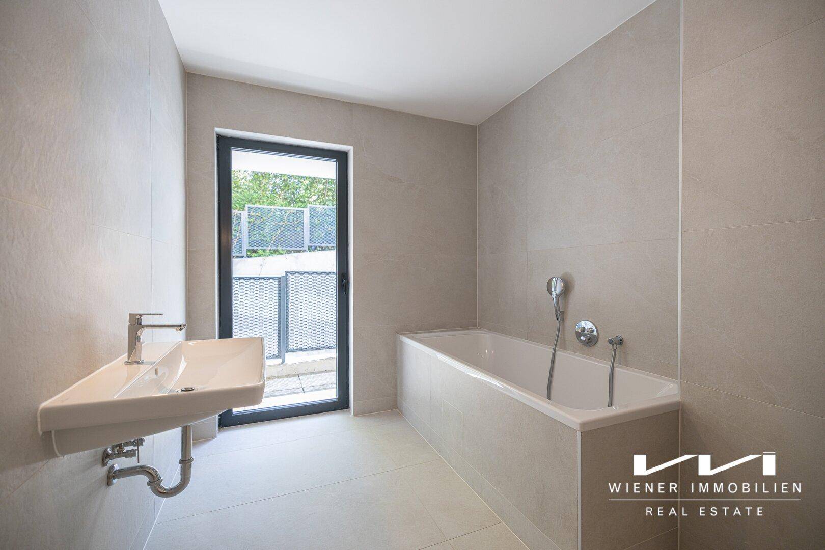 Modernes Badezimmer mit hellgrauen Fliesen, Badewanne und großem Fenster für Tageslicht.