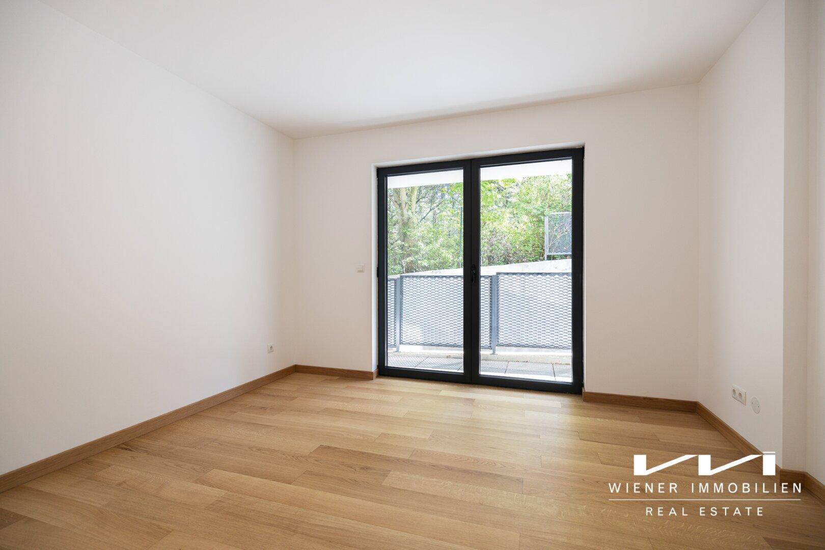 Helles Schlafzimmer mit Parkettboden und Zugang zu einem kleinen Balkon oder Terrasse.
