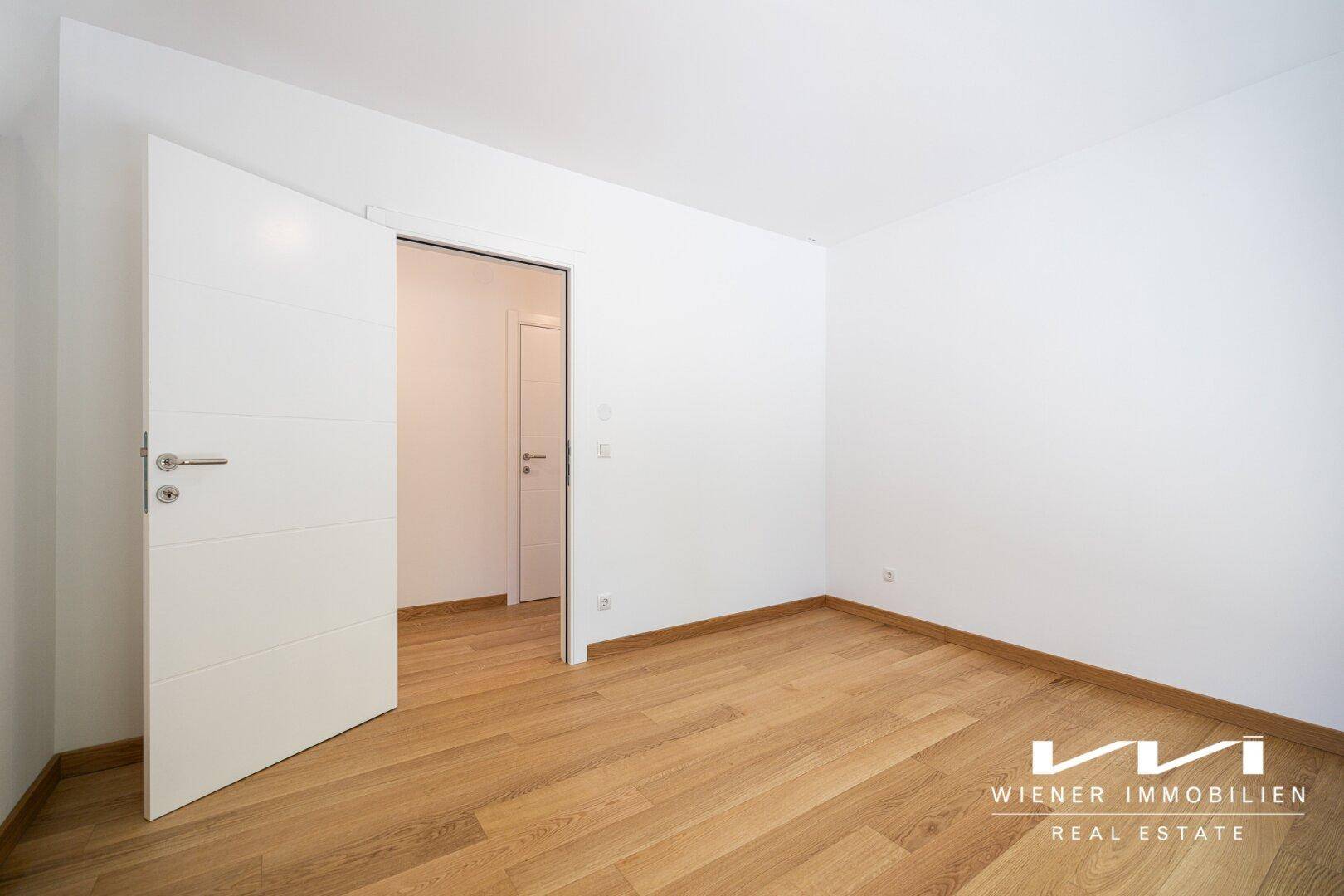 Helles Zimmer mit Parkettboden und moderner weißer Tür, bereit zur individuellen Gestaltung.