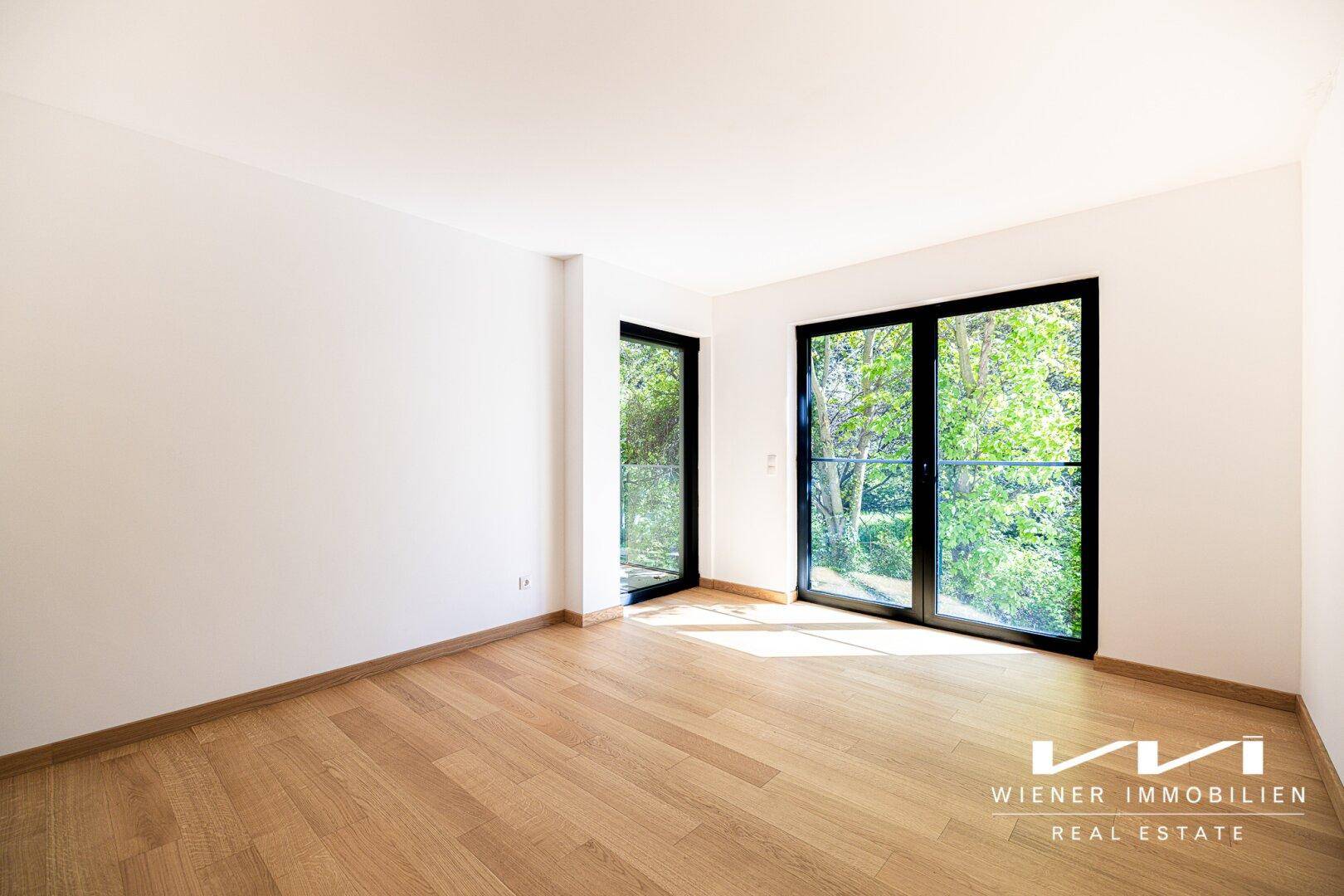 Helles Schlafzimmer mit Holzboden und großen Fenstern, die einen schönen Blick ins Grüne bieten.