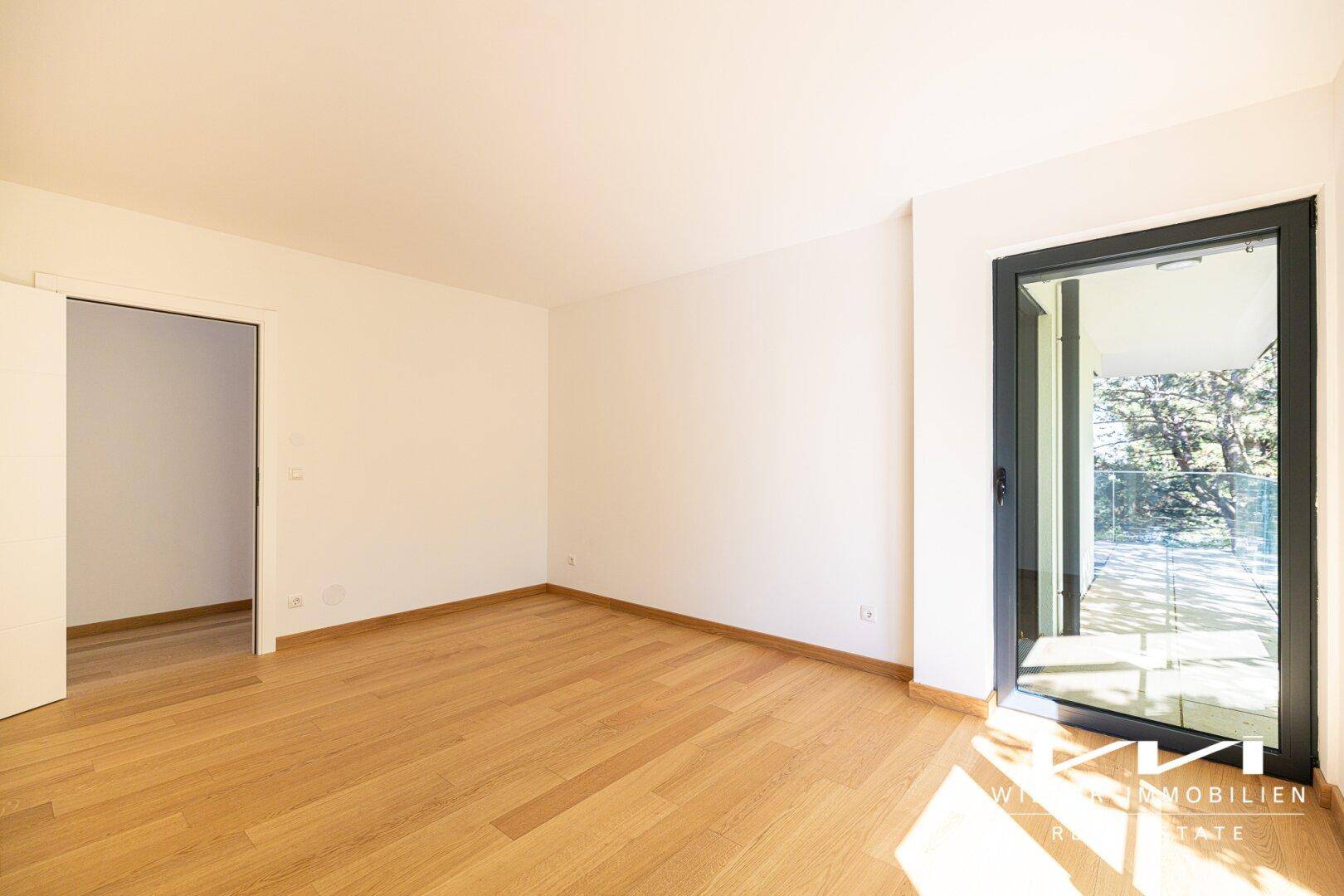 Lichtdurchflutetes Zimmer mit Eichenparkett und Zugang zu einem privaten Balkon.