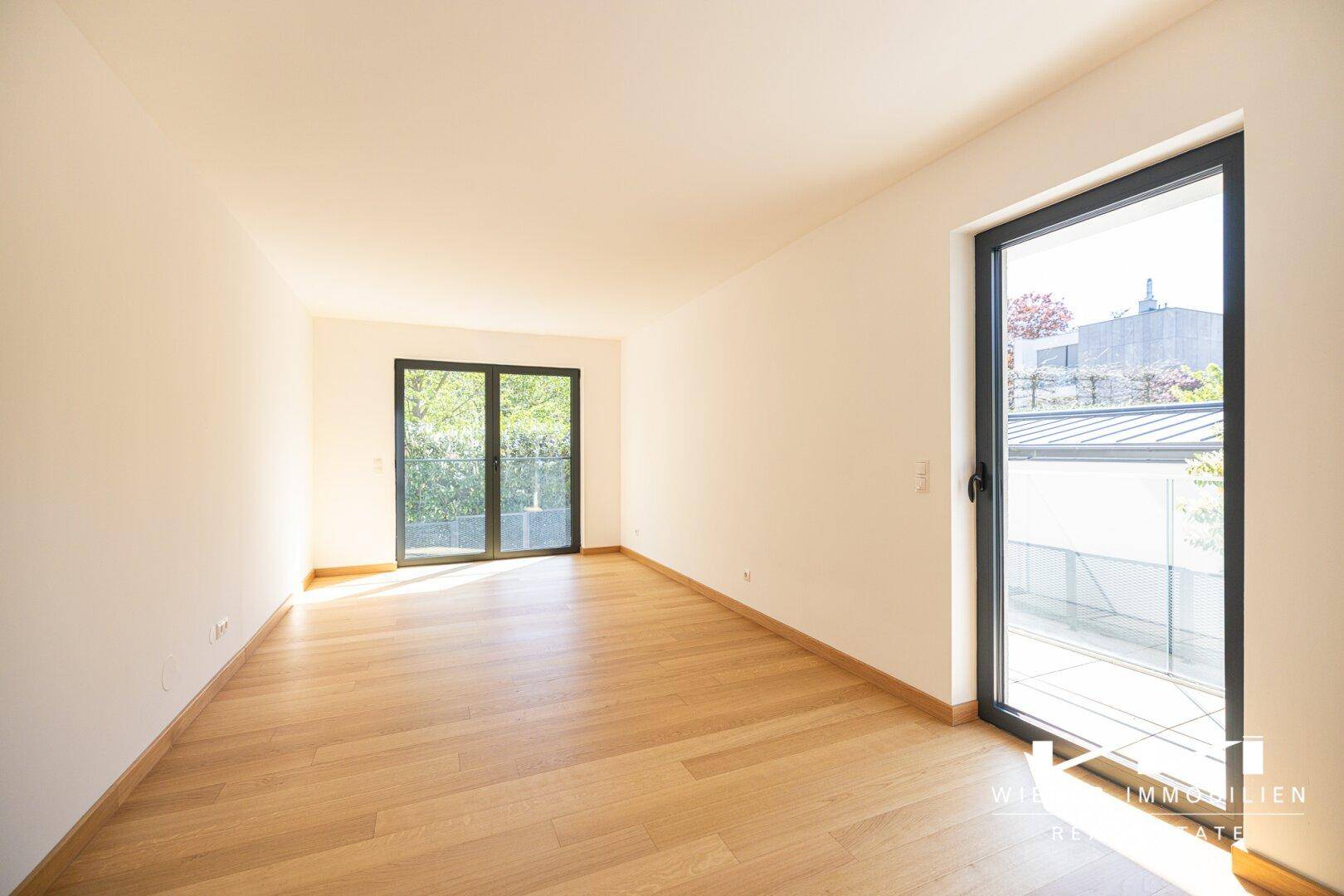 Helles Zimmer mit Holzboden und großen Fenstern, die viel Sonnenlicht hereinlassen.