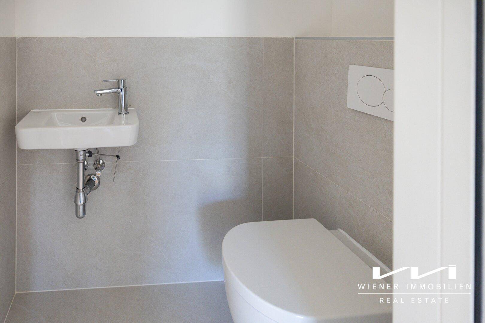 Modernes Gäste-WC mit wandhängender Toilette und kleinem Waschbecken in neutralen Farbtönen.