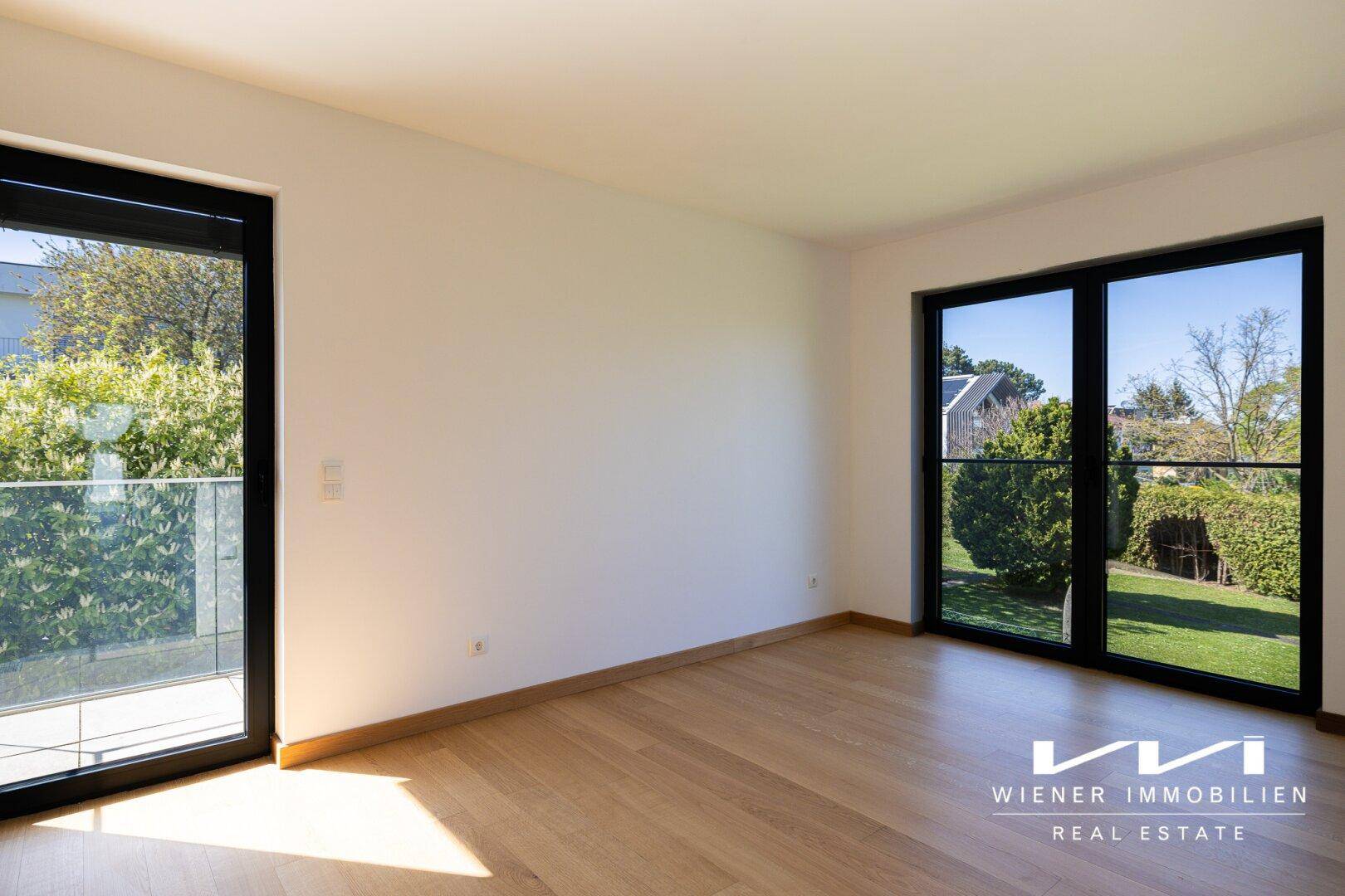 Heller Raum mit Holzboden und Zugang zu einem französischen Balkon mit Blick ins Grüne.
