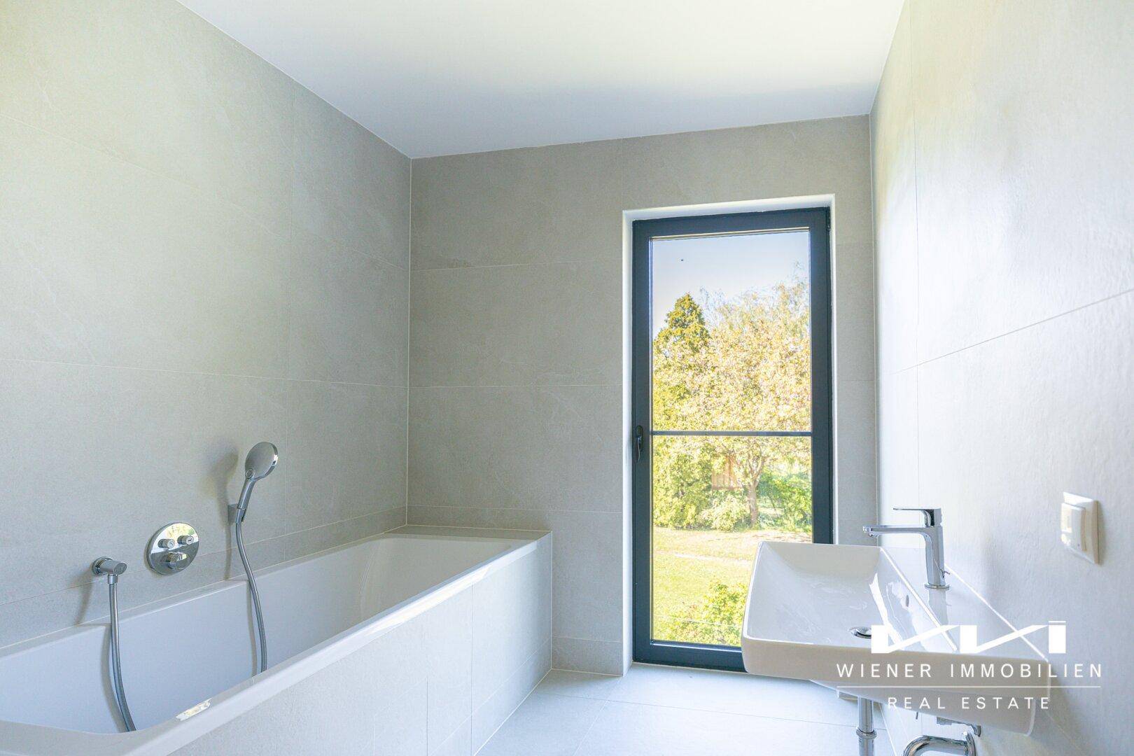 Helles Badezimmer mit Badewanne, modernem Waschbecken und Fenster mit Blick ins Grüne.