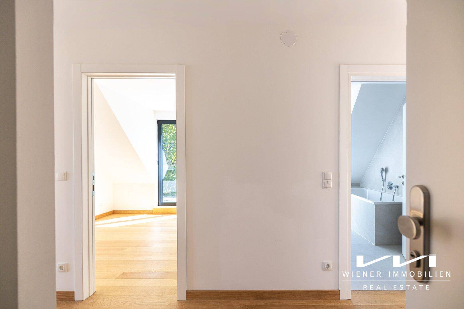 Heller Flur mit zwei offenen Türen, die zu einem Zimmer und einem modernen Badezimmer führen.