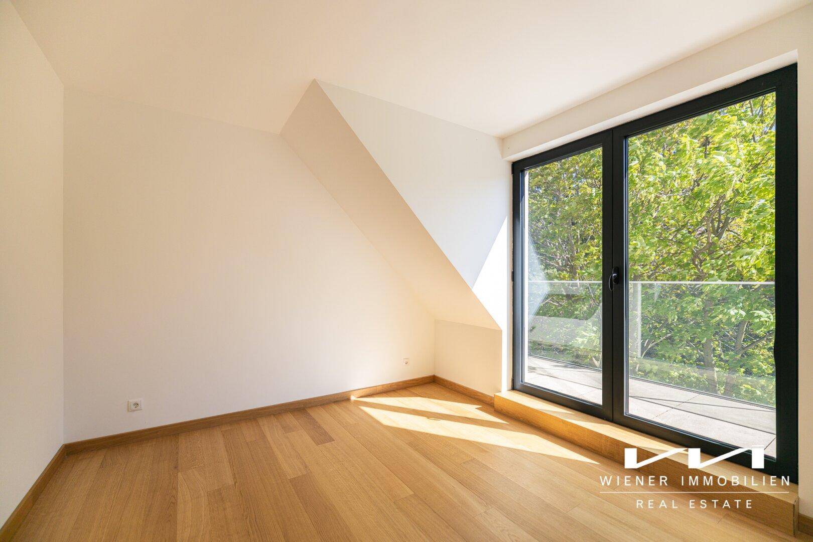 Helles Schlafzimmer mit Holzboden, schräger Decke und großem Fenster mit Zugang zu einem Außenbereich.