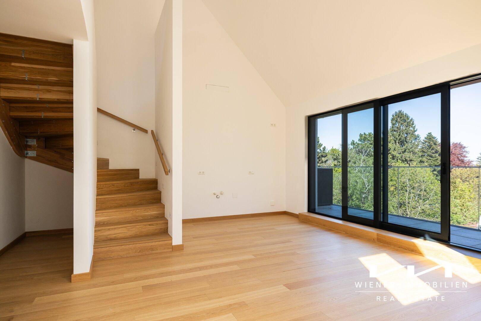Heller Raum mit Holztreppe, Parkettboden und großen Fenstern mit Zugang zu einem Außenbereich.