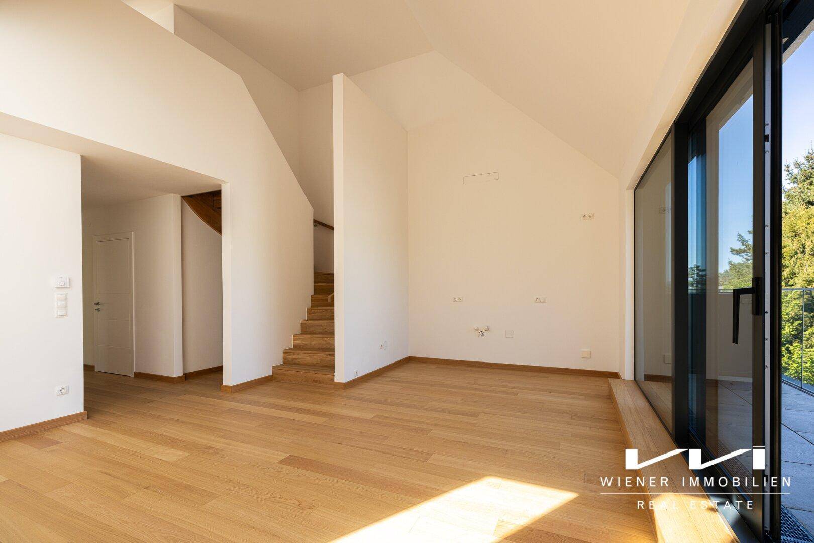 Geräumiger, heller Raum mit Holzboden, großen Fenstern und Blick auf eine moderne Holztreppe.