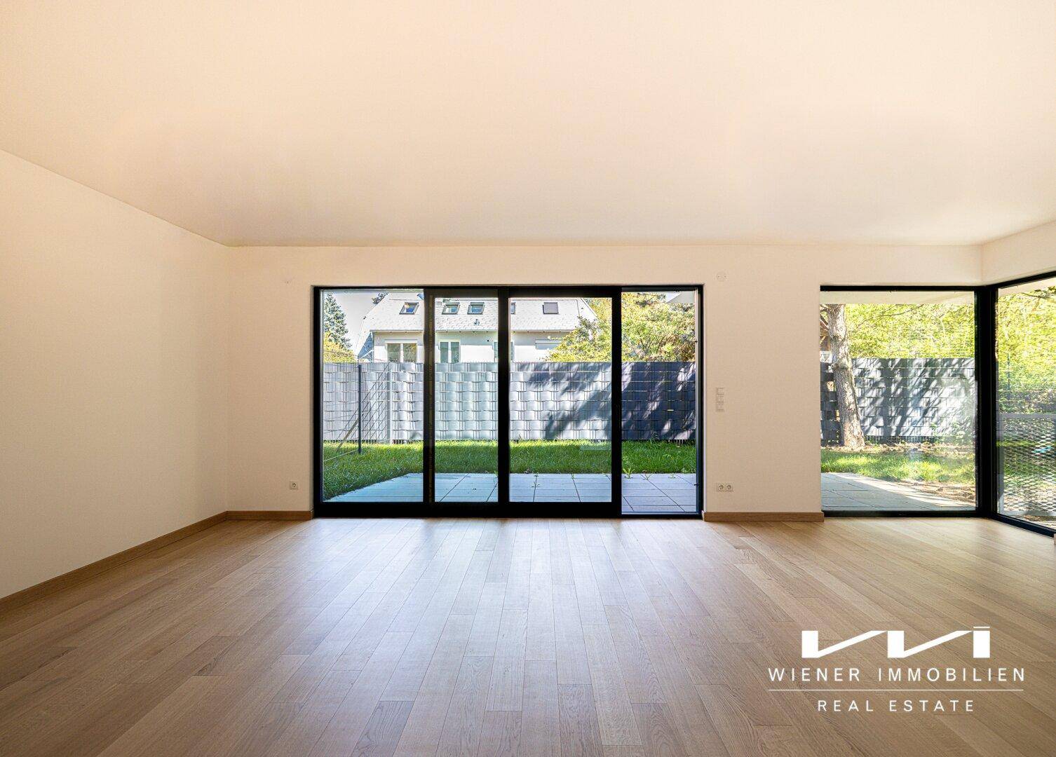 Weitläufiges Wohnzimmer mit viel Tageslicht durch große Fenster und Blick ins Grüne.