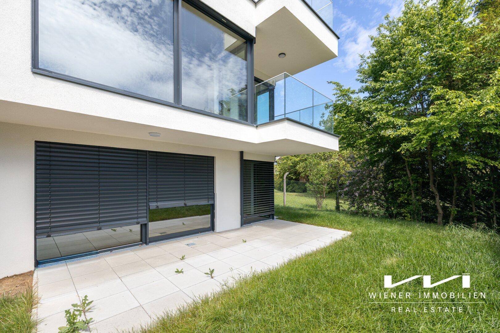 Erdgeschoss-Terrasse mit direktem Zugang zum grünen Gartenbereich des modernen Gebäudes.