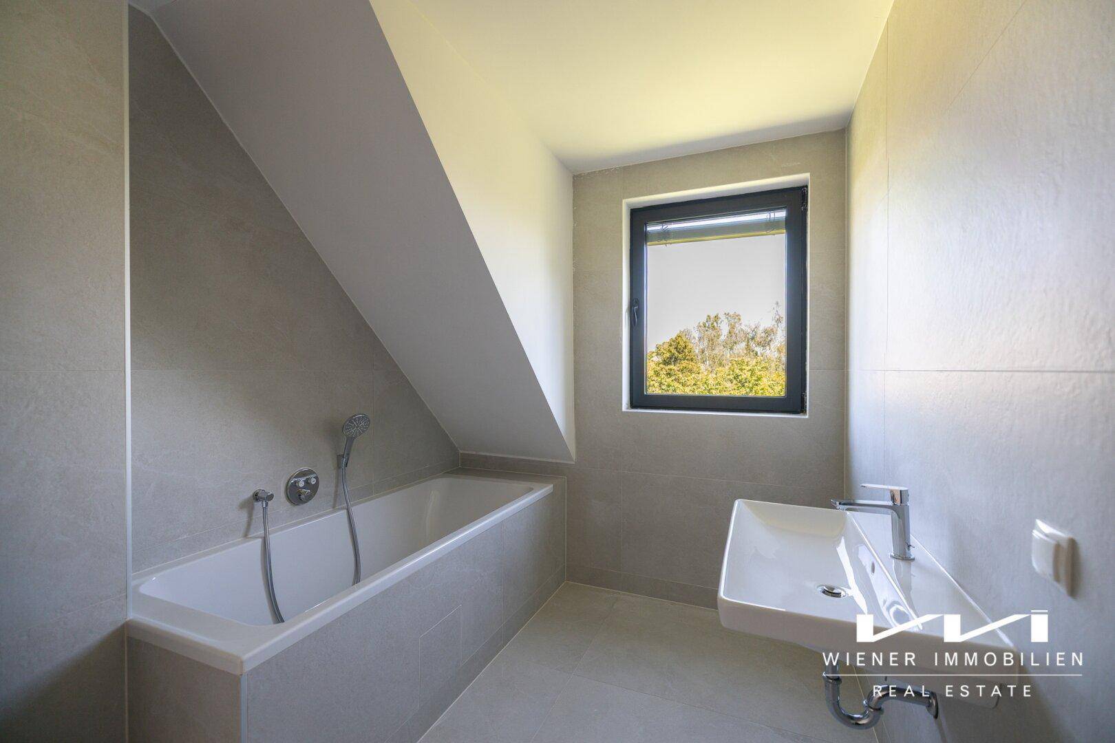 Modernes Badezimmer mit Badewanne, Fenster und hellgrauen Fliesen.