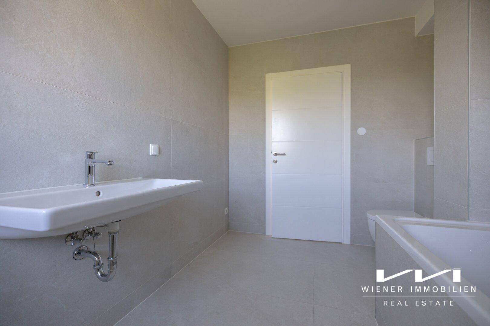 Helles Badezimmer mit Waschbecken, Badewanne und modernen grauen Fliesen.