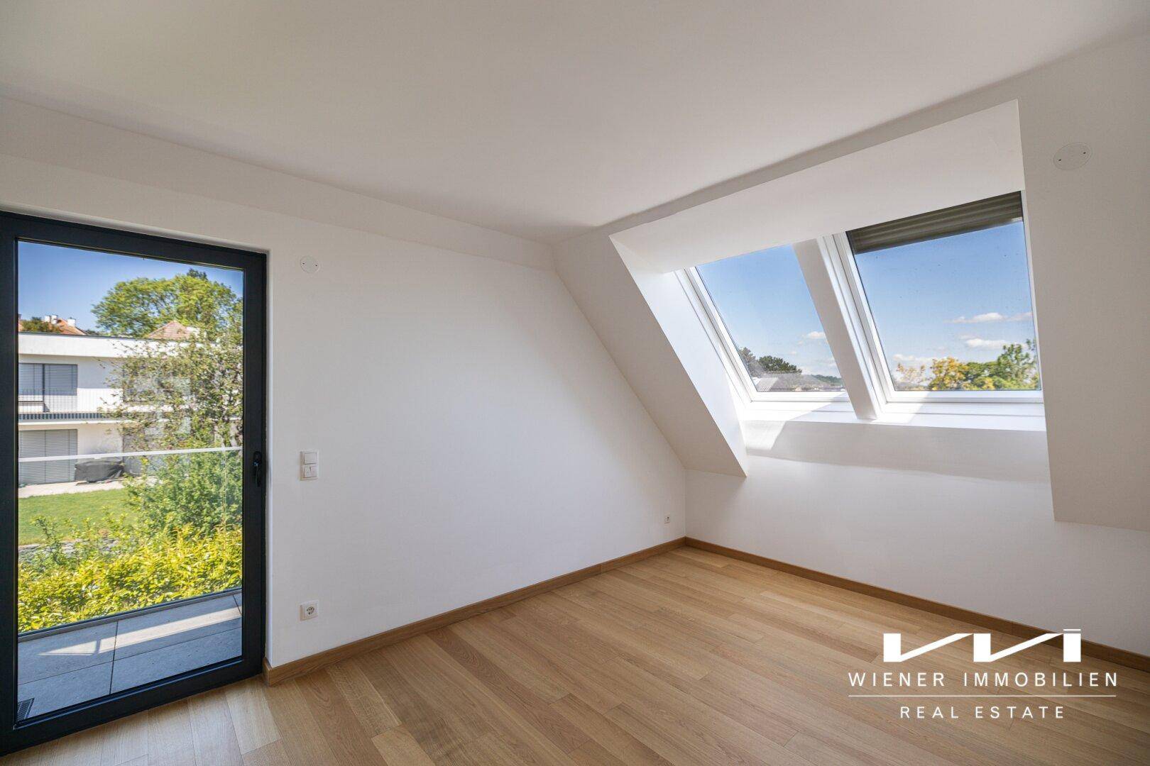 Helles Zimmer im Dachgeschoss mit Holzboden, Dachfenstern und Zugang zum Balkon.