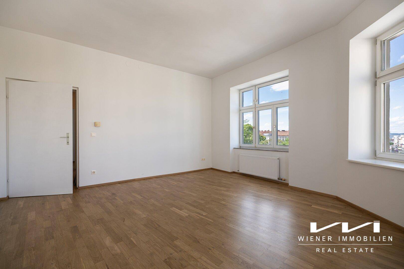 Helles Zimmer mit Parkettboden und zwei Fenstern, bietet viel Tageslicht.