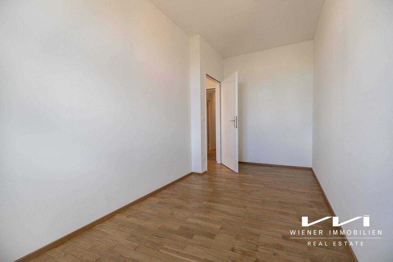 Leeres Zimmer mit Parkettboden und offener Tür, bietet flexible Nutzungsmöglichkeiten.