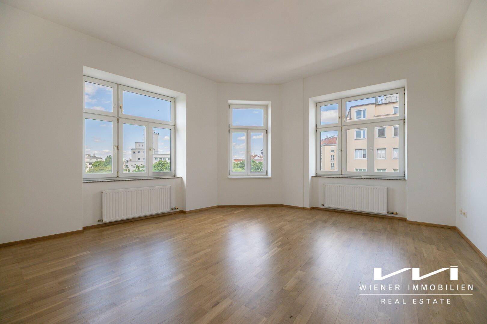 Geräumiges, leeres Wohnzimmer mit Parkettboden und großen Fenstern, bereit zur Gestaltung.
