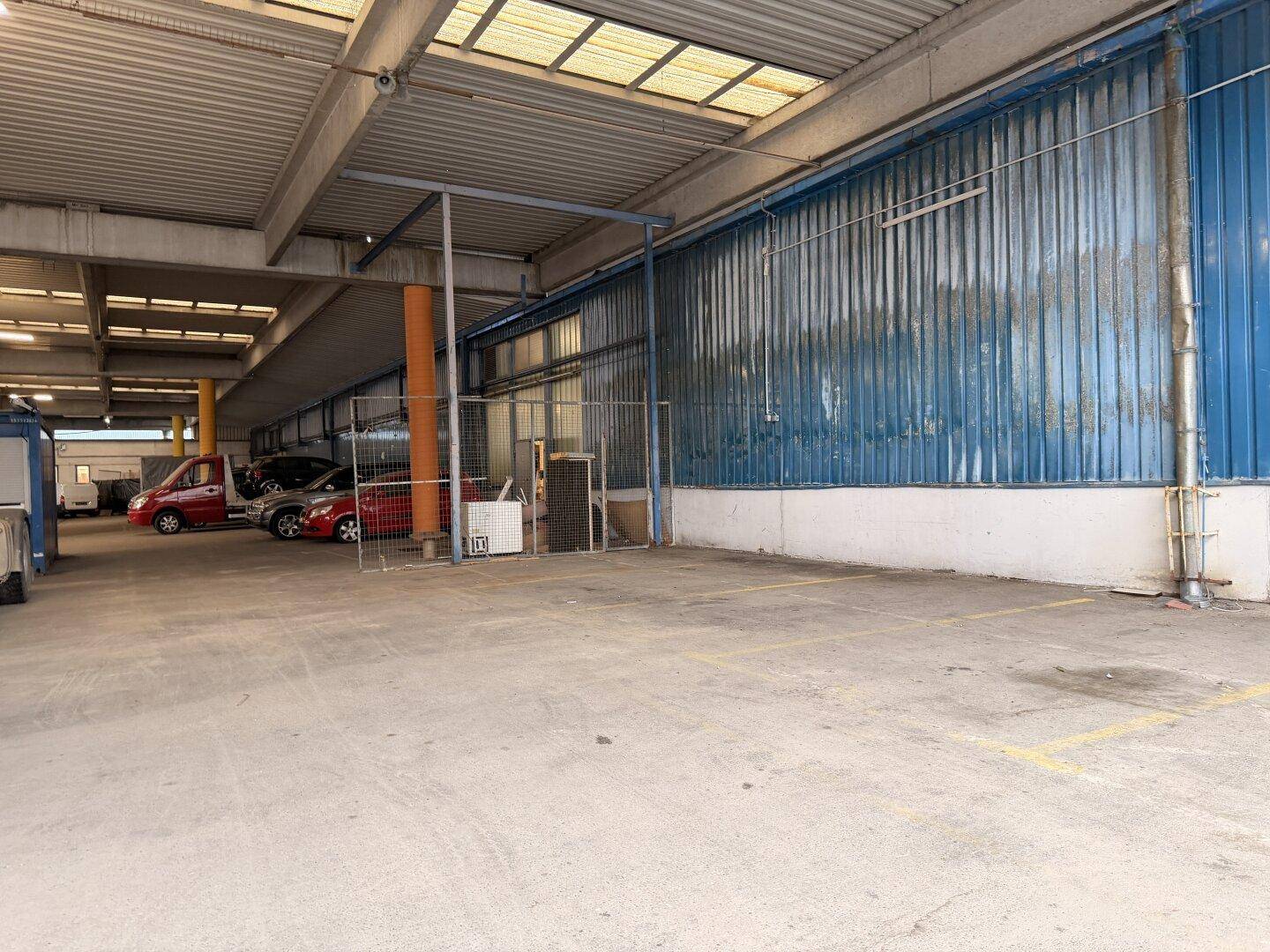 Außenparkplatz mit markierten Stellflächen neben einem blauen Industriegebäude, ideal für Fahrzeuge.